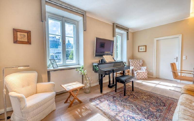 Helles Wohnzimmer mit Klavier, Holzboden und weitem Blick aus den großen Fenstern.