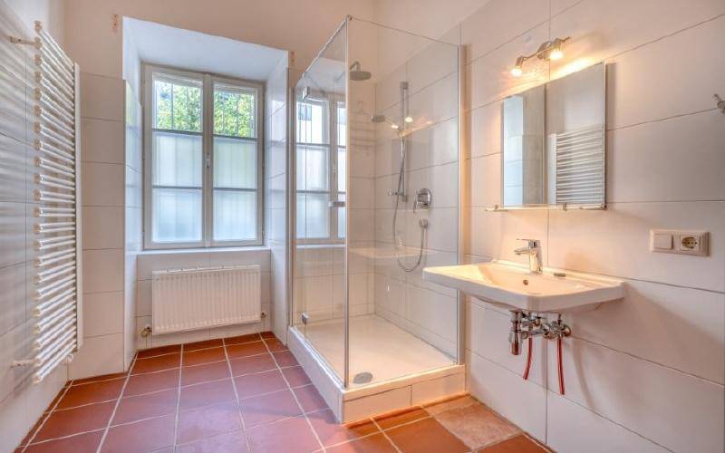 Helles Badezimmer mit moderner Glasdusche, beheiztem Handtuchhalter und Fenster für Tageslicht.