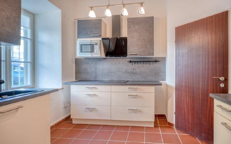 Moderne Küche mit grauen und weißen Schränken, Induktionskochfeld und Terrakottafliesen am Boden.