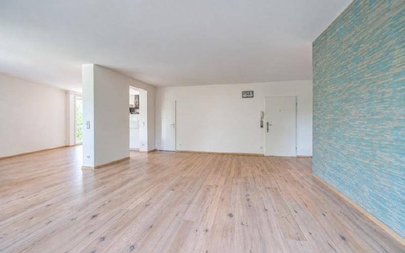 Geräumiger Wohnbereich mit Parkettboden und einer Wand in Blautönen.
