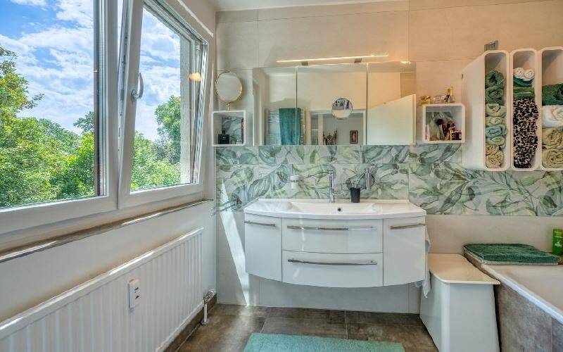 Modernes Badezimmer mit Fenster, Waschtisch und floraler Wandgestaltung.