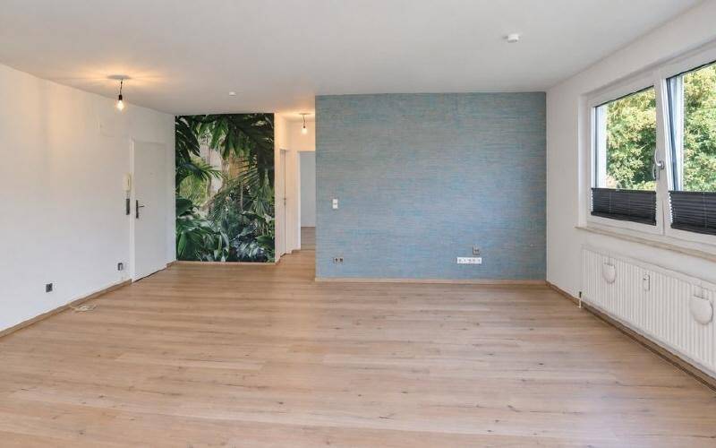 Heller Wohnbereich mit Parkettboden, dekorativer Tapete und großem Fenster.