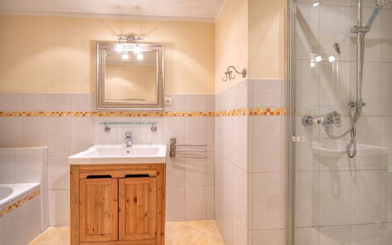 Funktionales Badezimmer mit Duschkabine, Waschtischunterschrank aus Holz und hellen Fliesen.