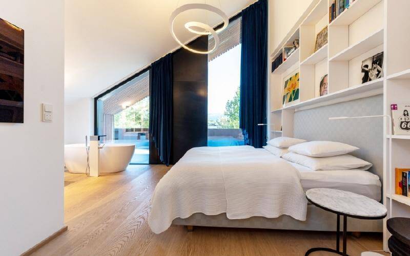 Helles Schlafzimmer mit Holzboden, Einbauregalen und freistehender Badewanne mit Aussicht.