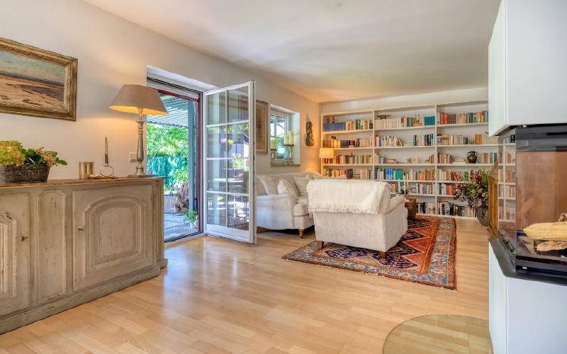 Helles Wohnzimmer mit Holzboden, großem Bücherregal und direktem Zugang zum Gartenbereich.