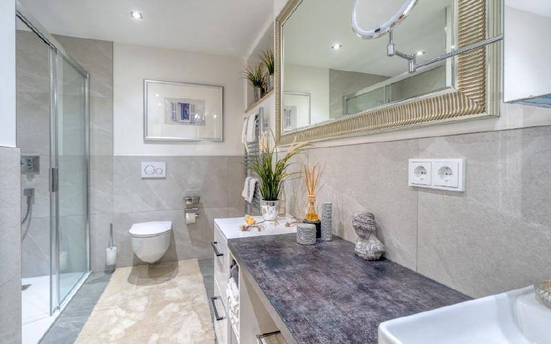 Modernes Badezimmer mit begehbarer Dusche, großem Spiegel und eleganten grauen Fliesen.