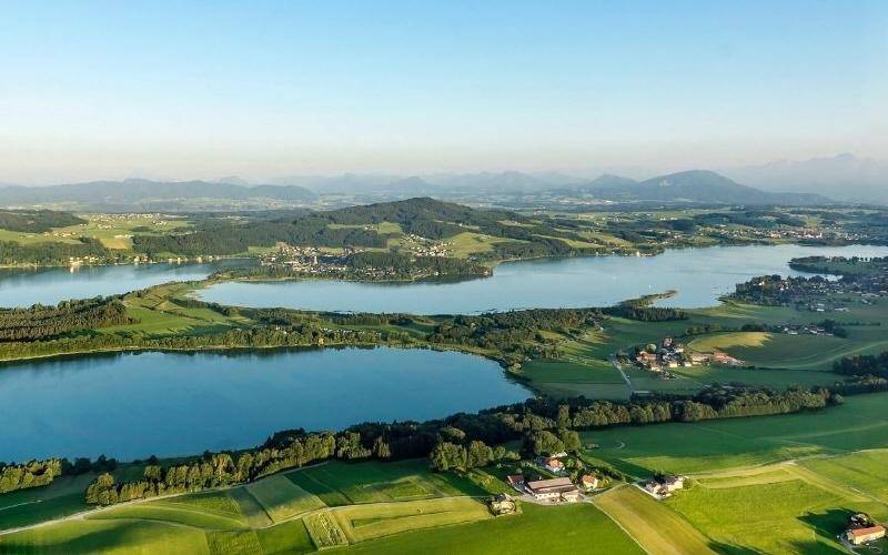 Panoramablick aus der Vogelperspektive auf mehrere Seen, umgeben von grünen Landschaften und Dörfern.