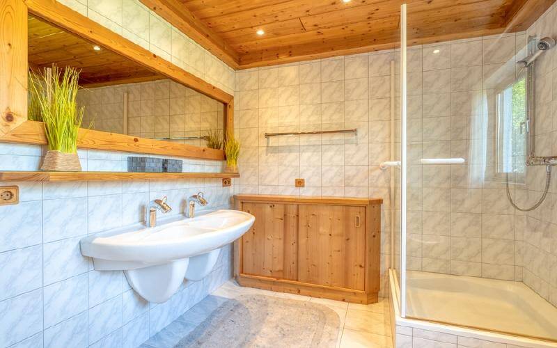 Helles Badezimmer mit Doppelwaschbecken, Duschkabine und Holzverkleidung an Decke und Möbeln.