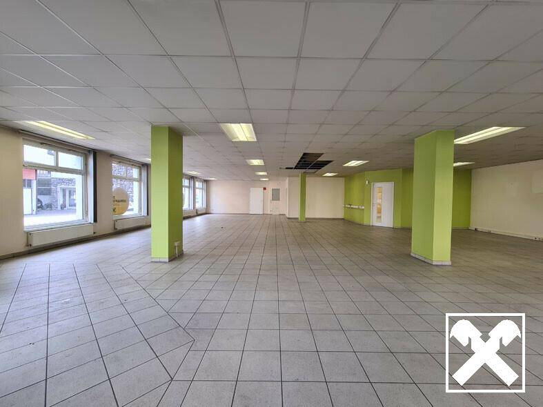 Weitläufiger Gewerberaum mit Fliesenboden, grünen Säulen und großen Fenstern, bietet vielseitige Nutzungsmöglichkeiten.