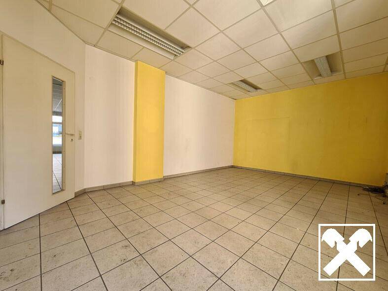 Heller Gewerberaum mit gelben Akzentwänden, Fliesenboden und Rasterdecke, ideal für Büros oder Ladenflächen.