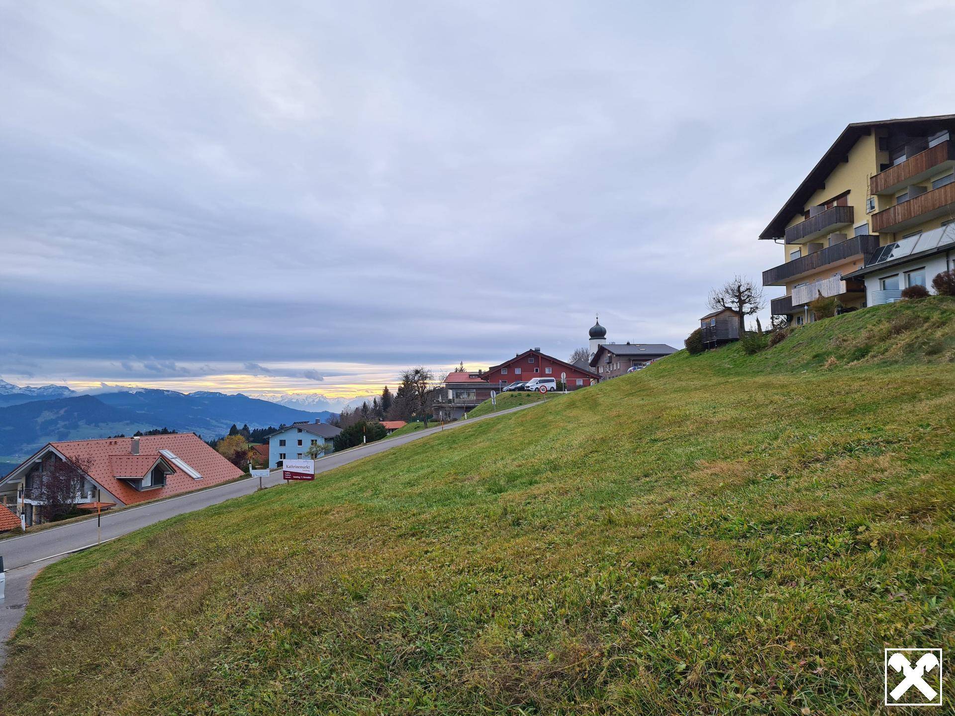 Blick auf eine Hanglage mit Wohnhäusern und Balkonen, umgeben von grüner Landschaft unter bewölktem Himmel.