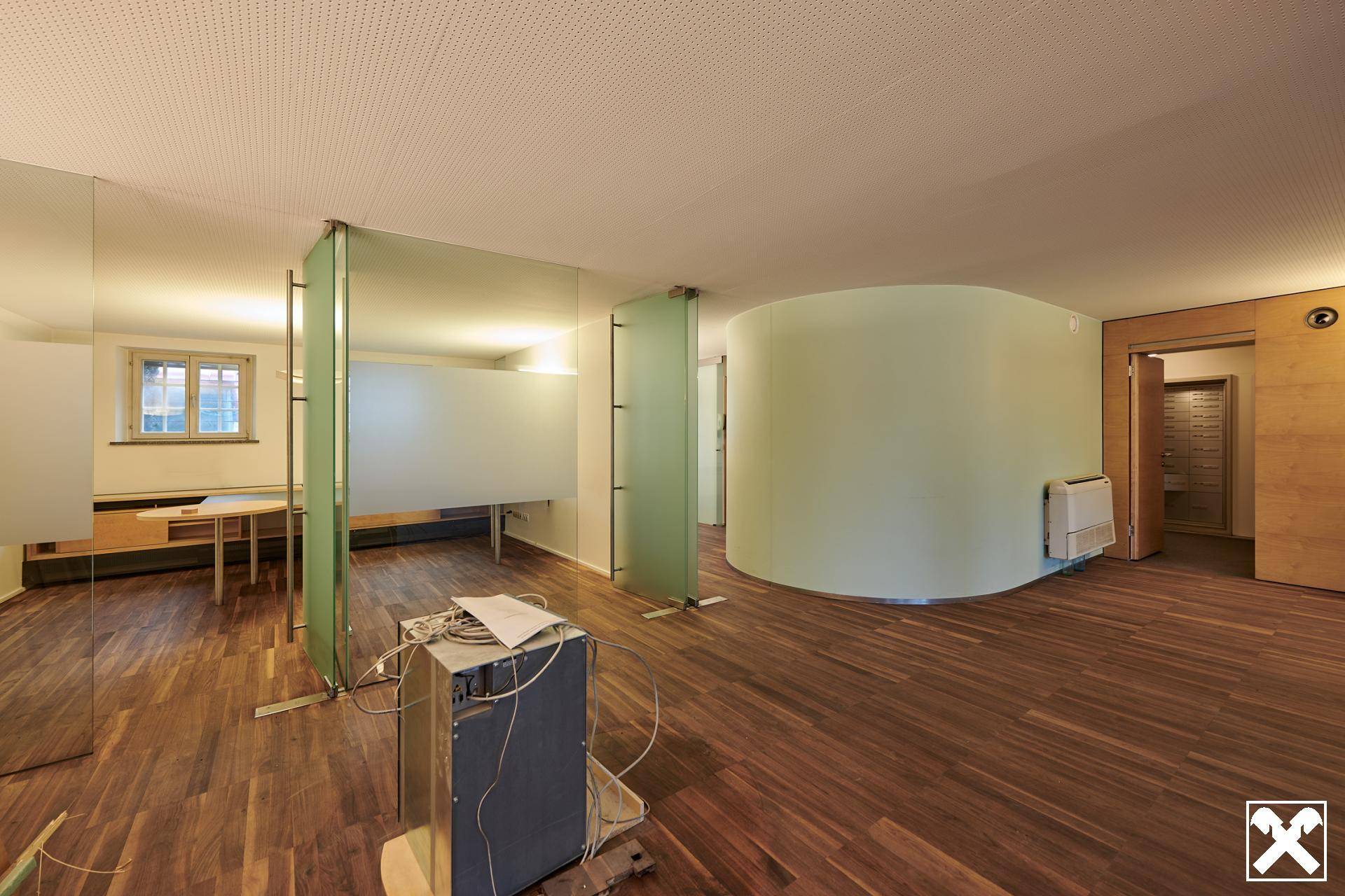 Offener Bürobereich mit Holzboden, geschwungenen Wänden und modernen Glasabtrennungen für flexible Arbeitsbereiche.