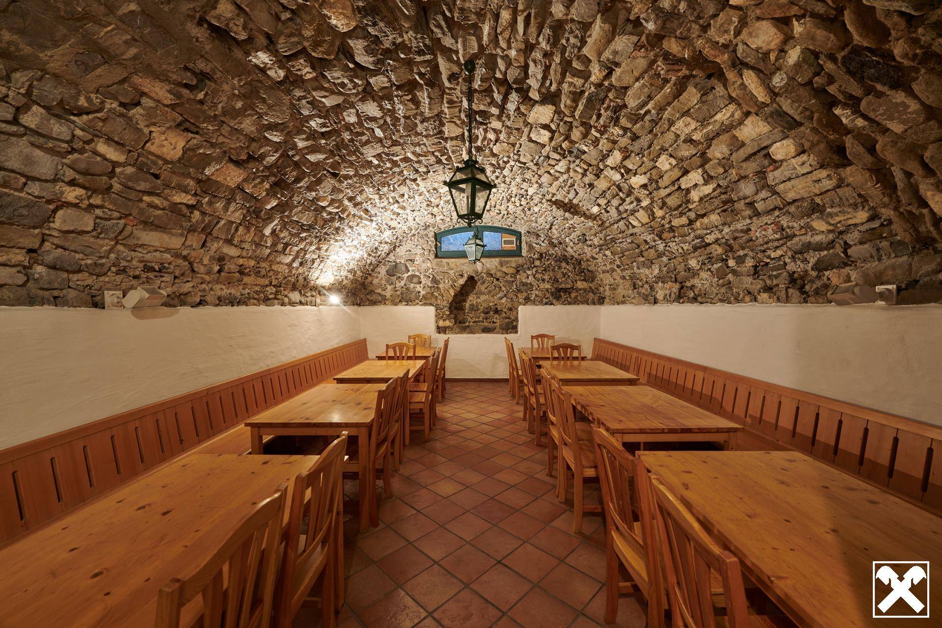 Rustikaler Restaurantkeller mit Gewölbedecke aus Naturstein, Terrakottafliesen und traditionellen Holztischen.