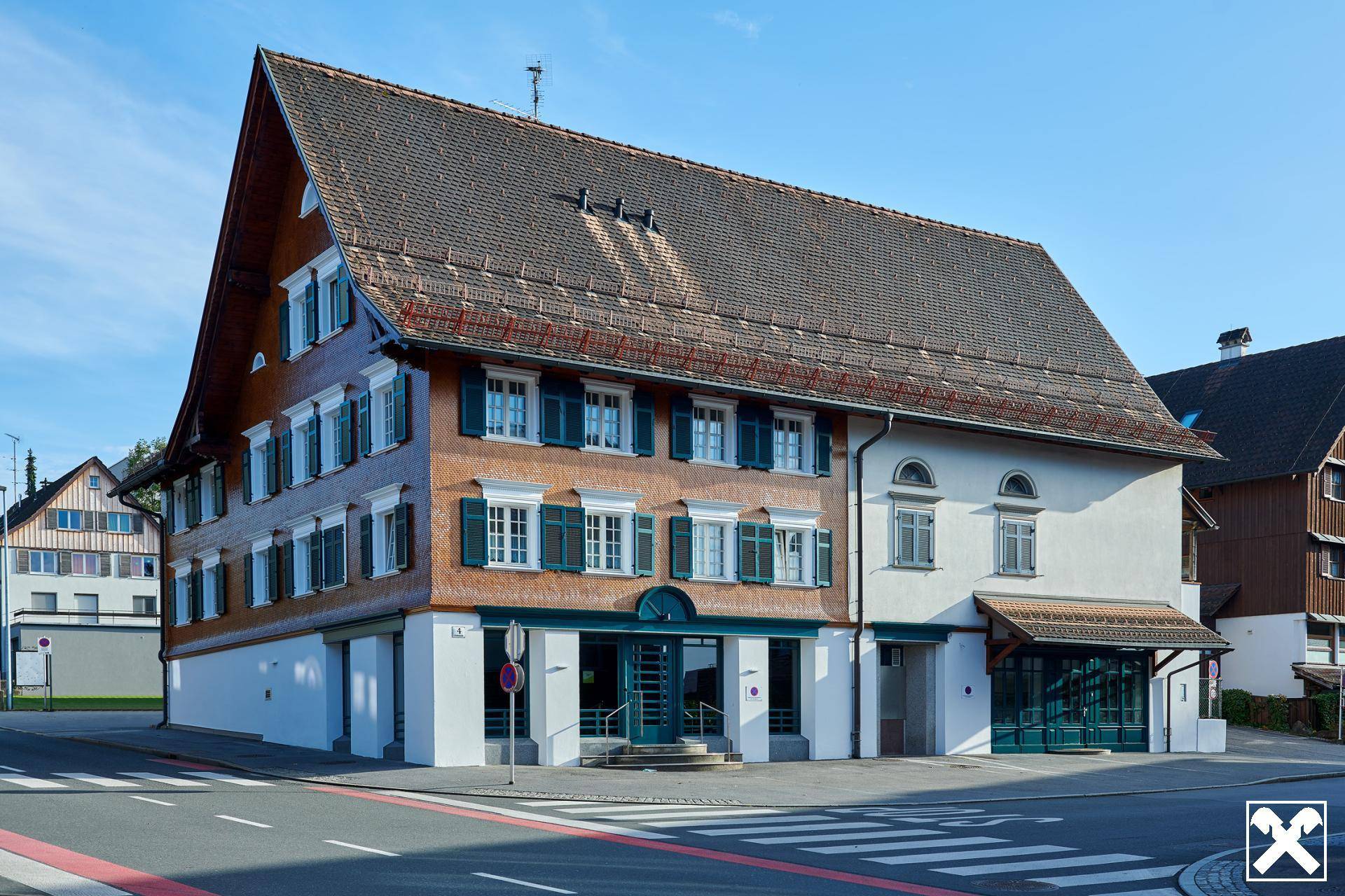 Traditionelles Gebäude mit Holz- und Putzfassade an einer Straßenecke unter blauem Himmel.