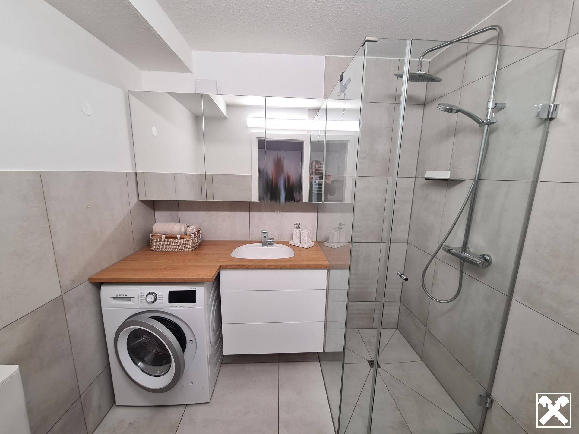 Modernes Badezimmer mit begehbarer Dusche, Waschbecken und integrierter Waschmaschine.