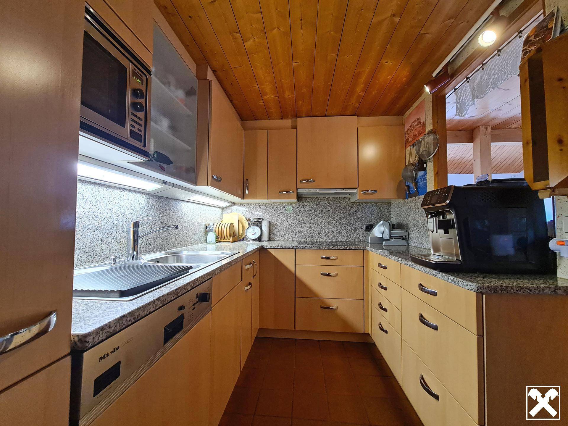 Funktionale Küche mit Holzschränken, Granitarbeitsplatten und modernen Einbaugeräten, inklusive Kaffeemaschine.