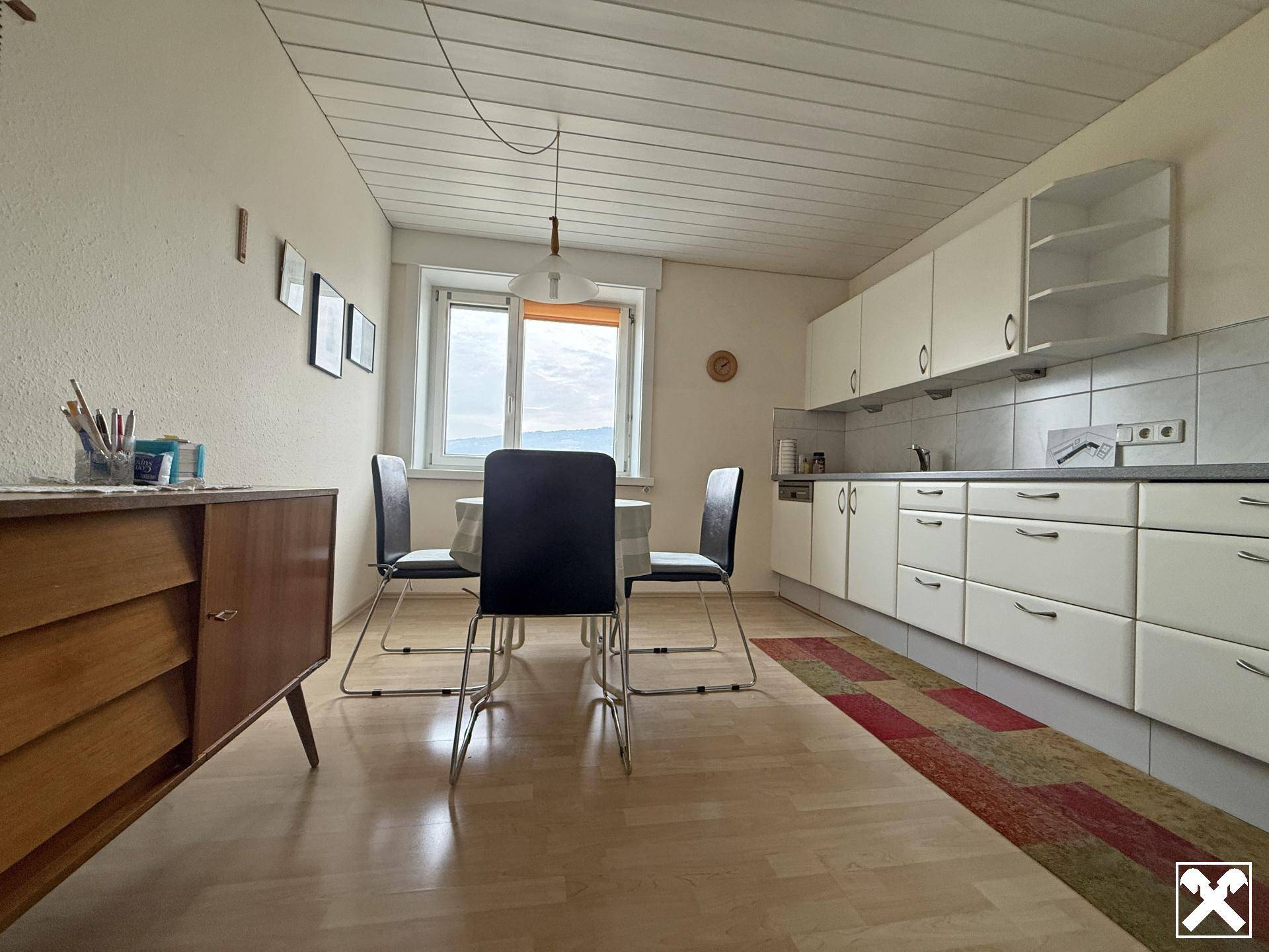 Wohnküche mit hellen Einbauschränken, Esstisch und Fenster mit Ausblick.