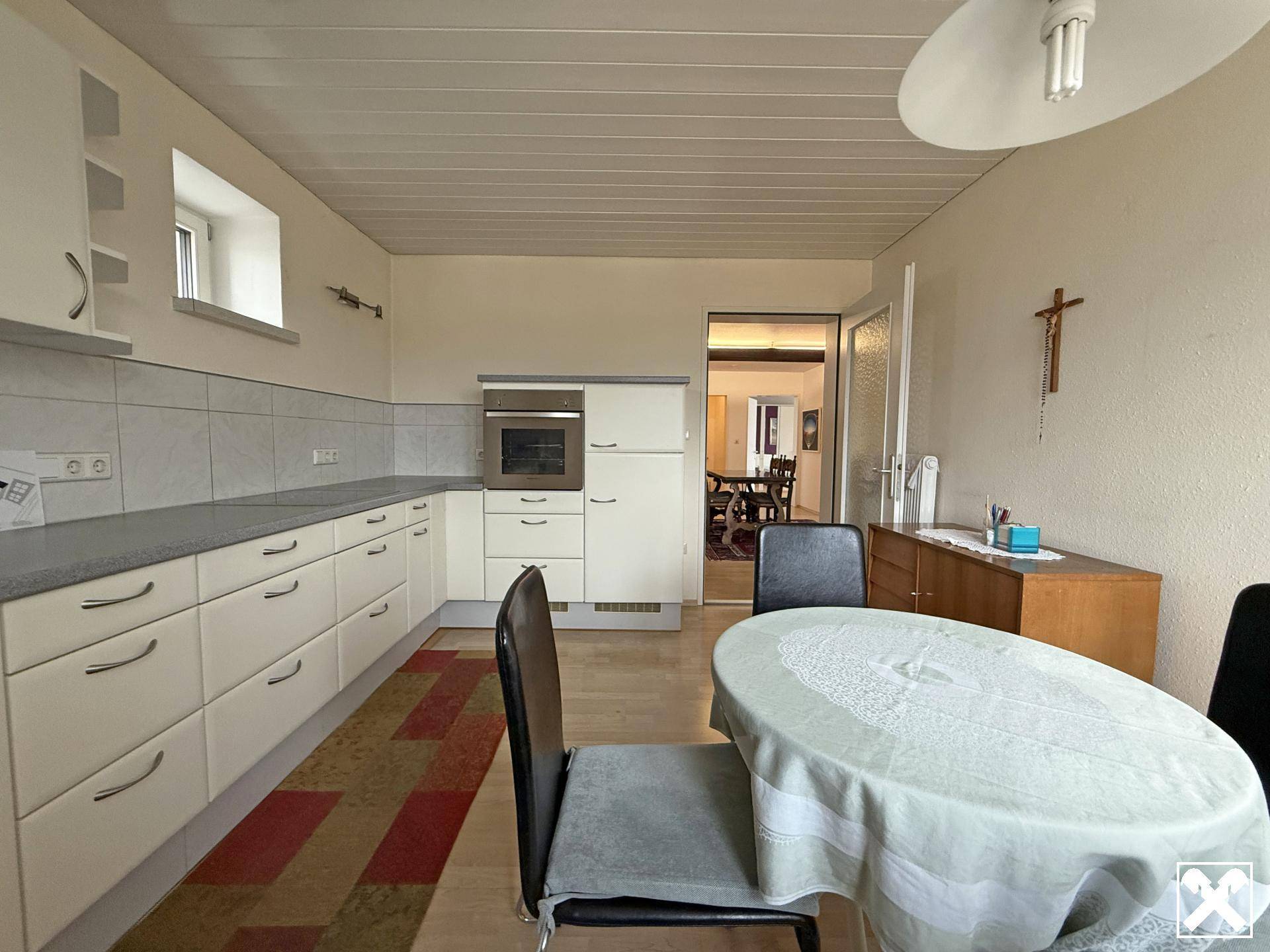 Funktionale Küche mit weißen Schränken, integriertem Backofen und Essbereich.