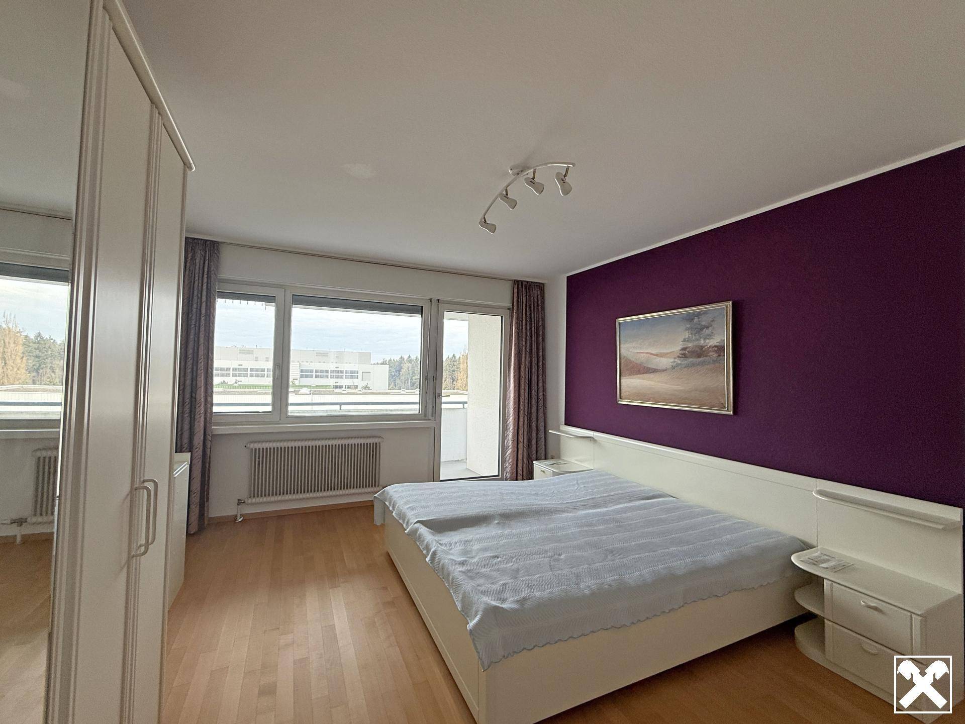 Schlafzimmer mit lila Akzentwand, Doppelbett und Zugang zum Balkon.