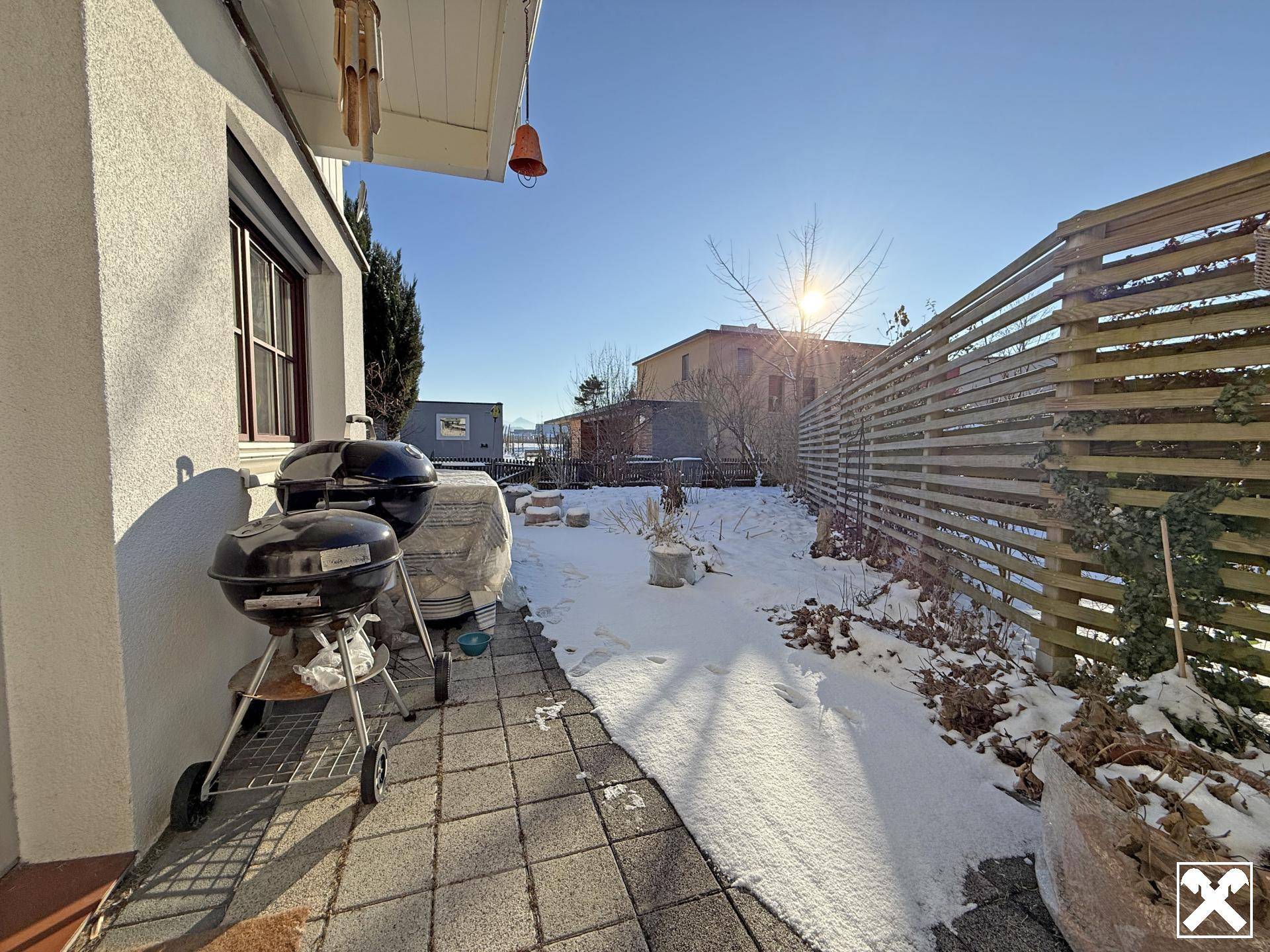 Sonniger Terrassenbereich mit Grillgeräten und Blick auf den verschneiten Garten.