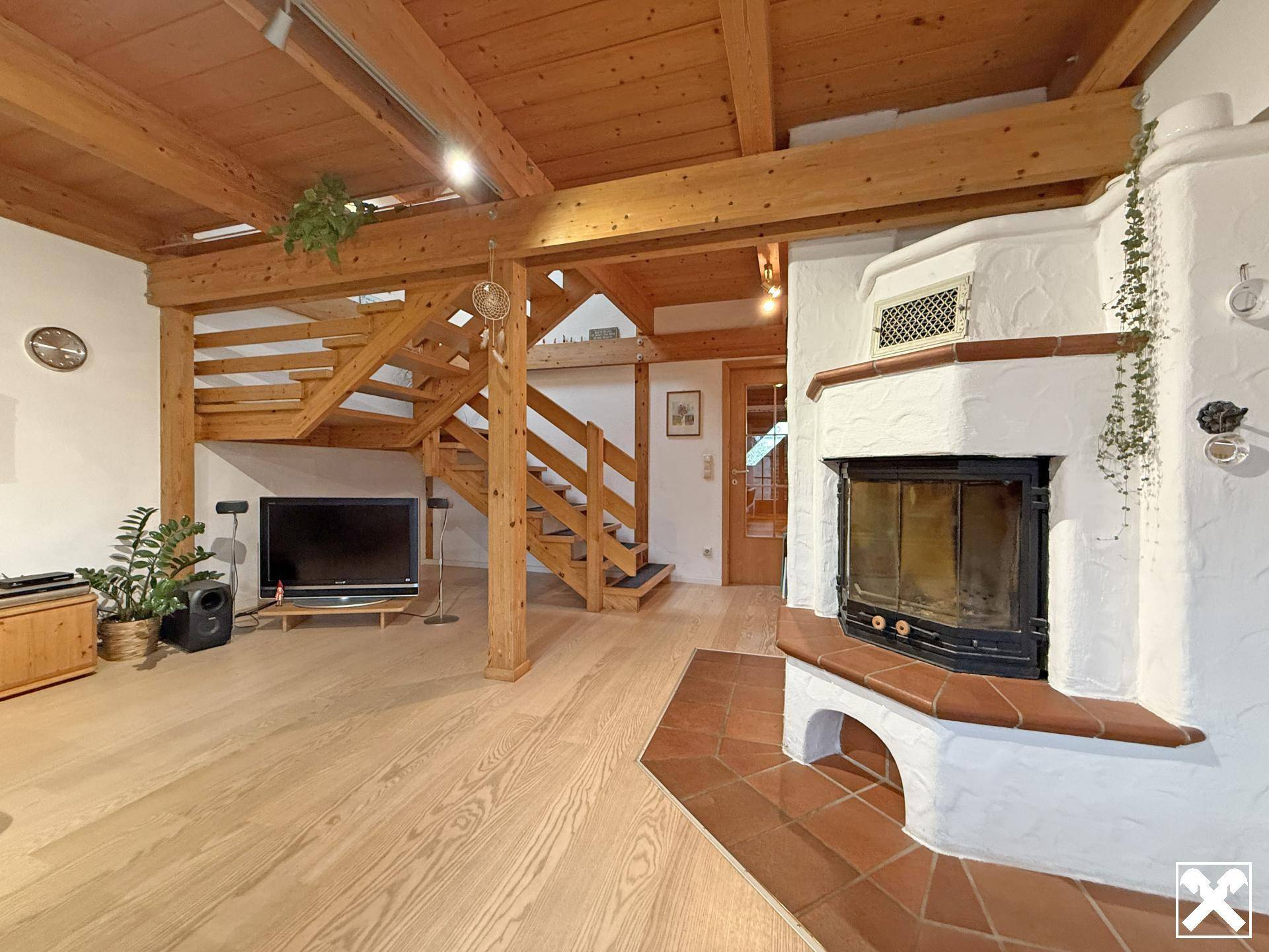 Gemütliches Wohnzimmer mit Holzbalkendecke, Kamin und offener Holztreppe zum Obergeschoss.