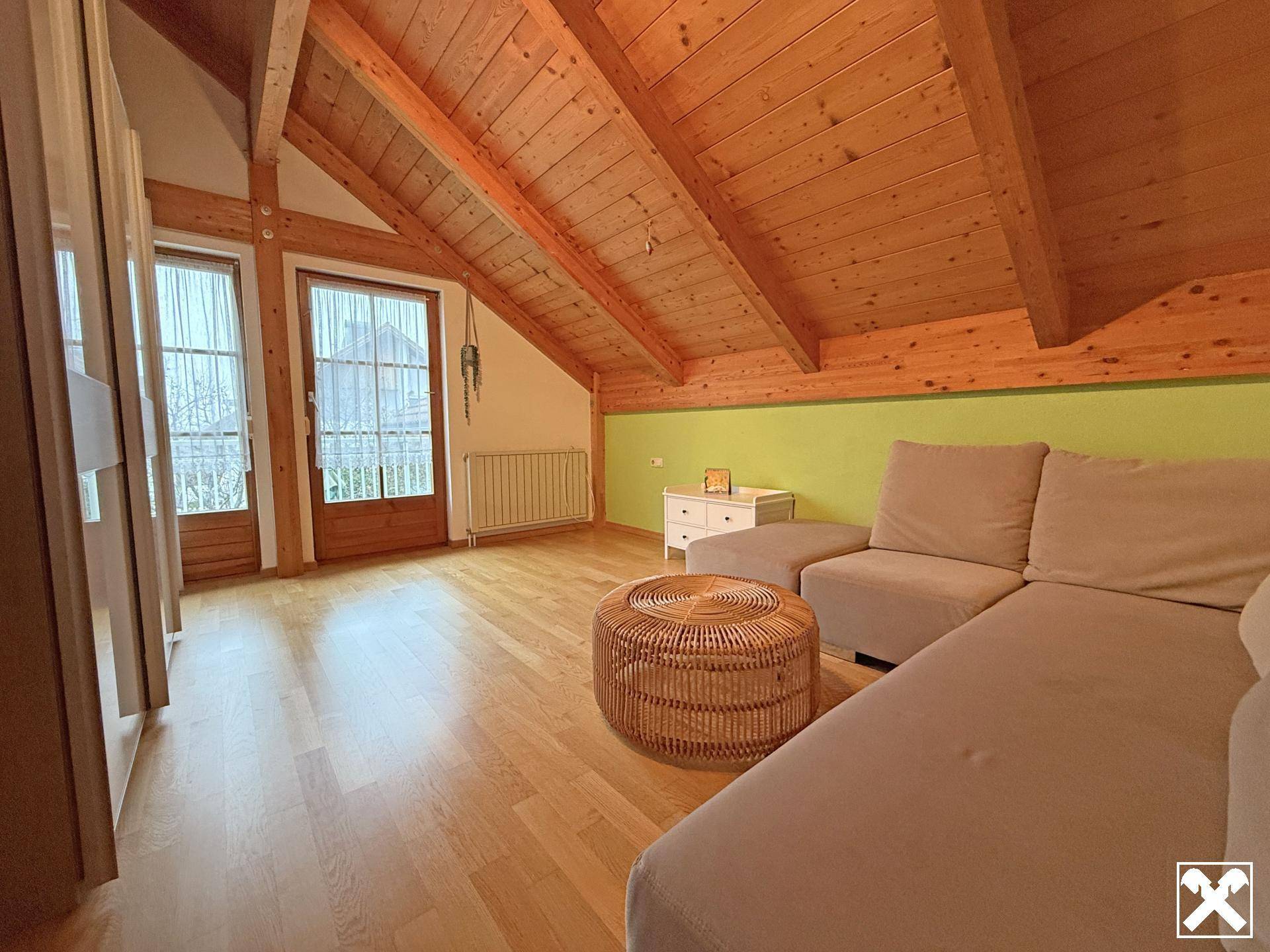 Heller Raum im Dachgeschoss mit Holzbalkendecke, Sofa und Zugang zu einem französischen Balkon.