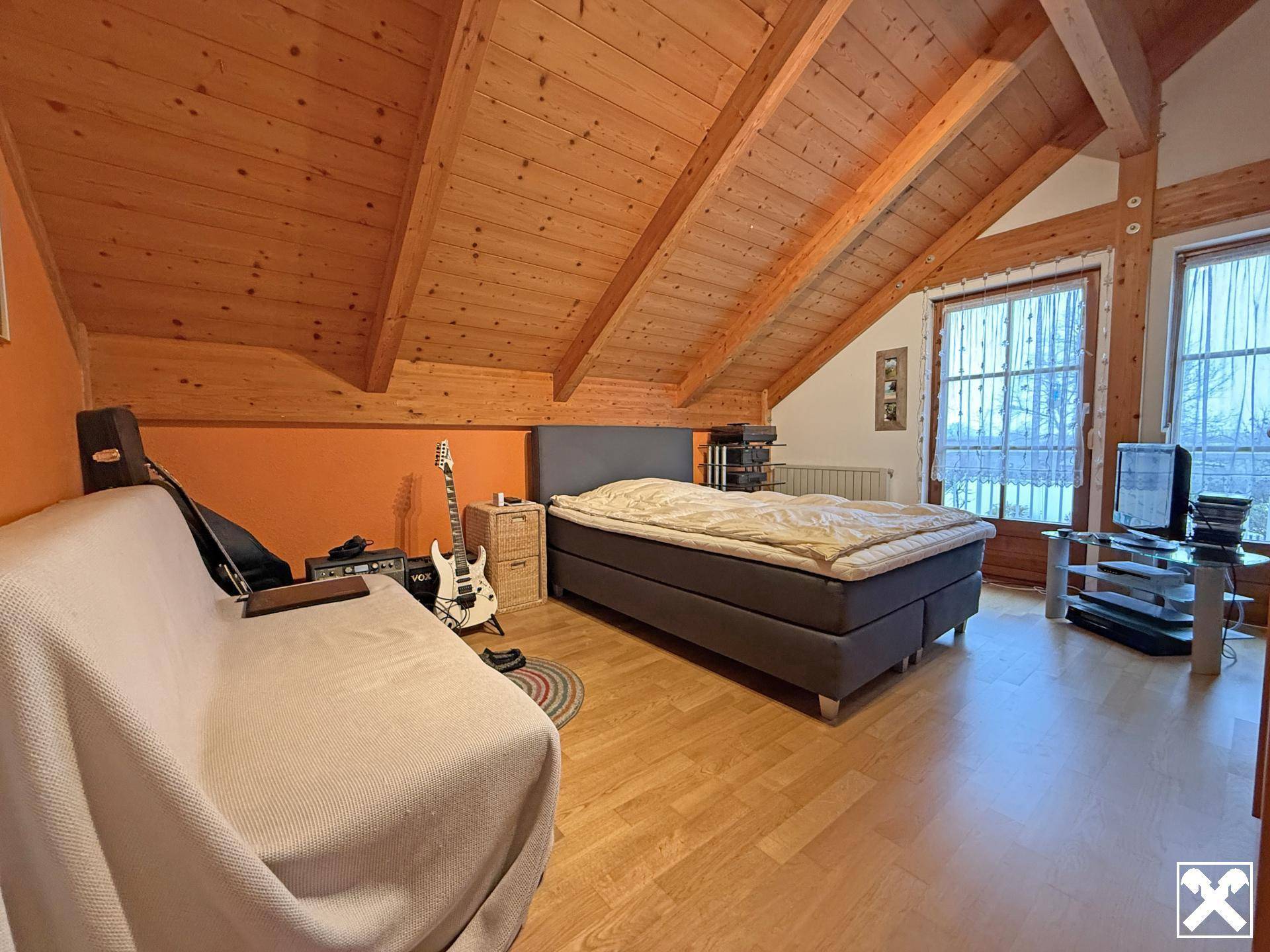 Geräumiges Schlafzimmer im Dachgeschoss mit Holzbalkendecke, Holzboden und großen Fenstern.