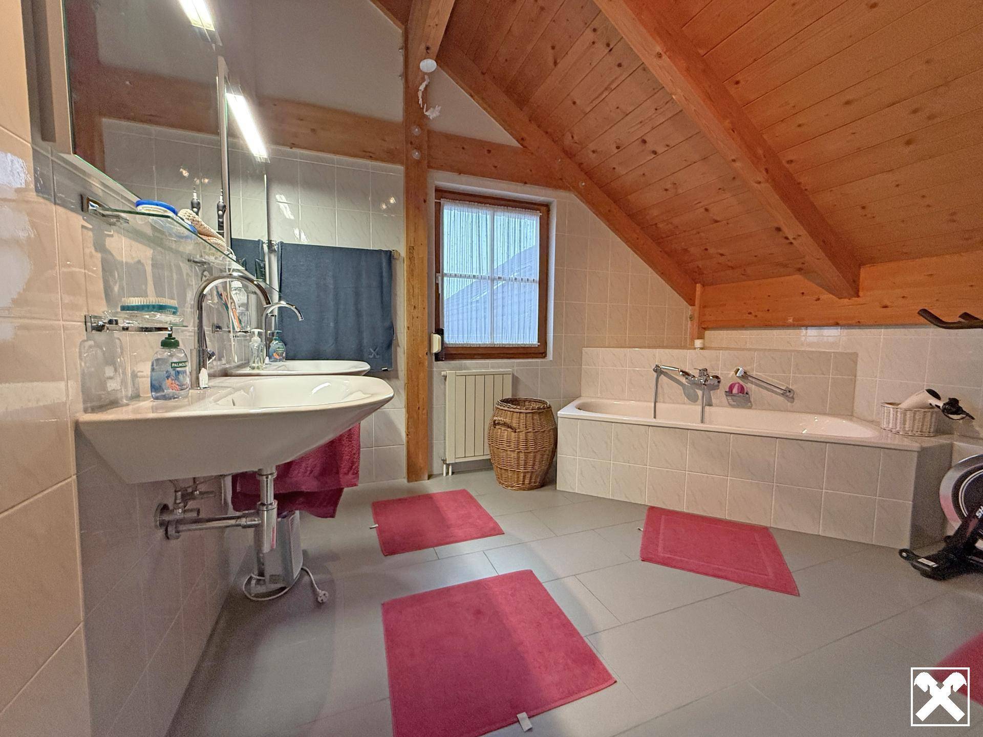 Helles Badezimmer im Dachgeschoss mit Badewanne, Doppelwaschbecken und Dachschräge.
