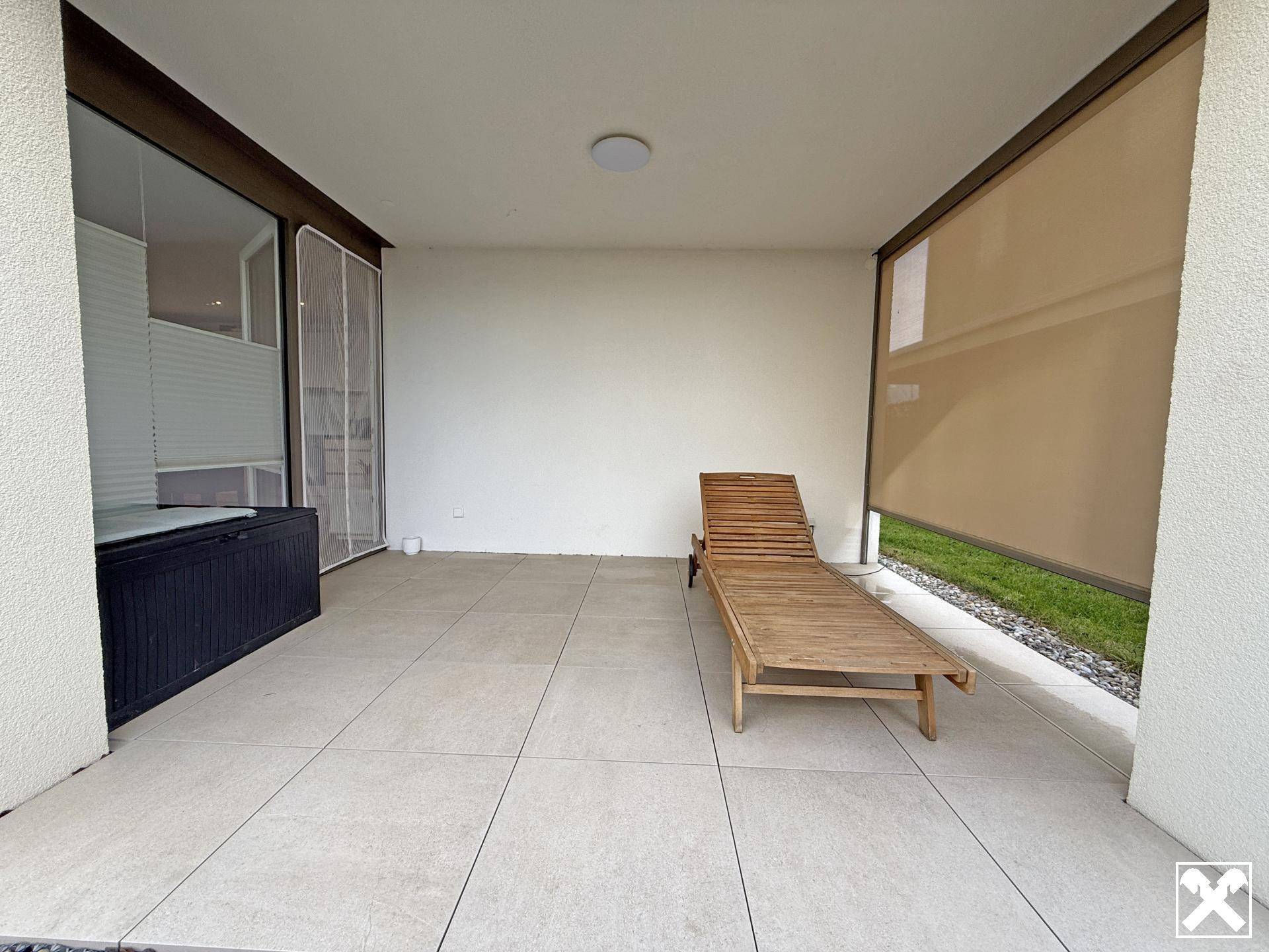Überdachte Terrasse mit Fliesenboden und einer Holzliege, ideal zum Entspannen im Freien und mit Sonnenschutz.