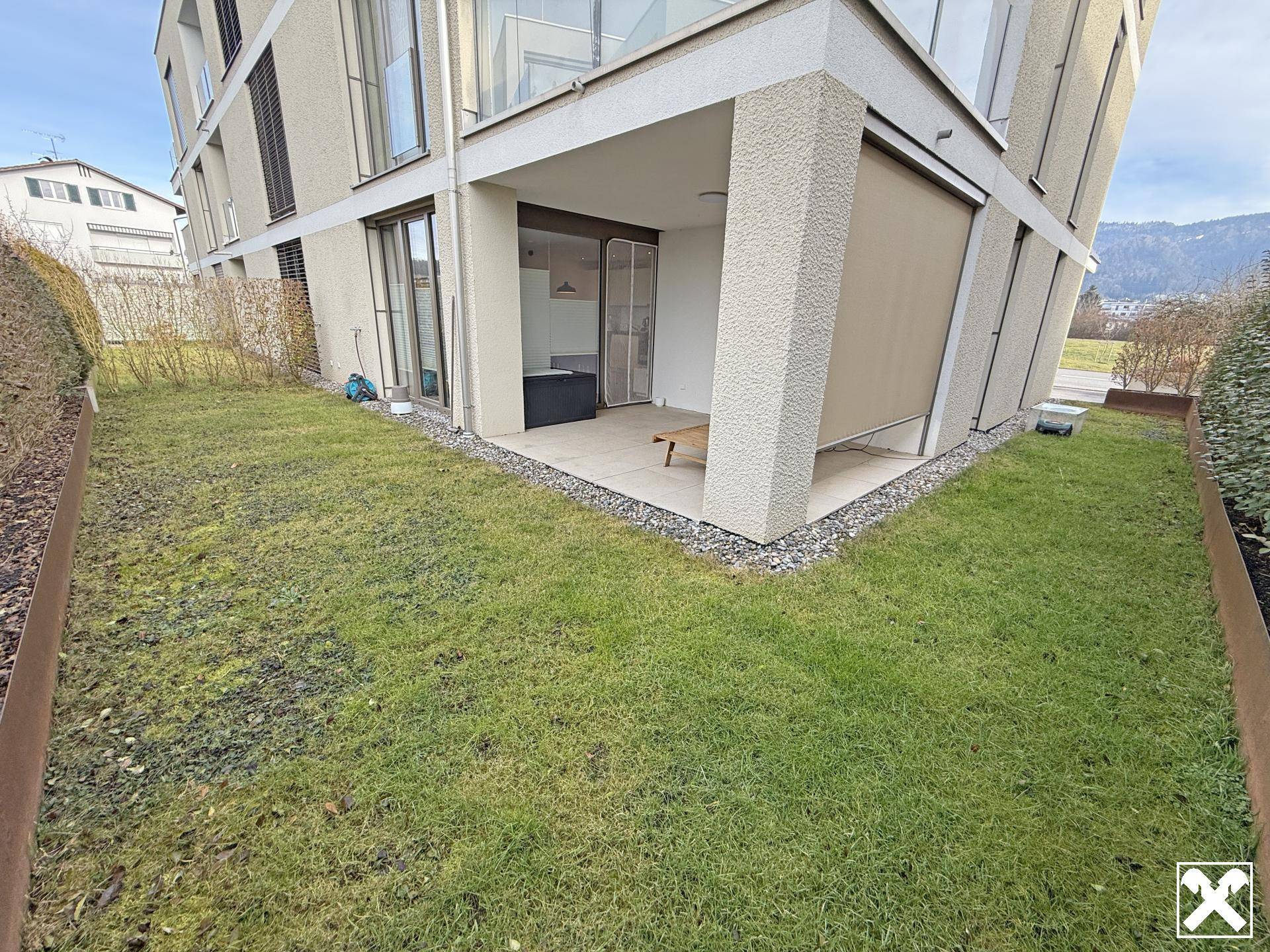 Gepflegter Gartenbereich mit Rasenfläche und Zugang zu einer überdachten Terrasse am modernen Gebäude.