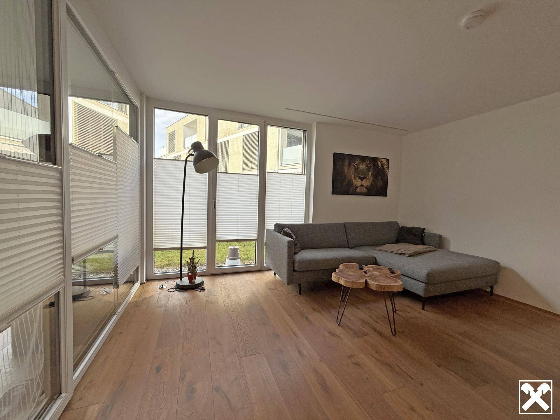 Gemütlicher Wohnbereich mit Sofa, Couchtisch und viel Tageslicht durch große Fenster mit Blick ins Grüne.