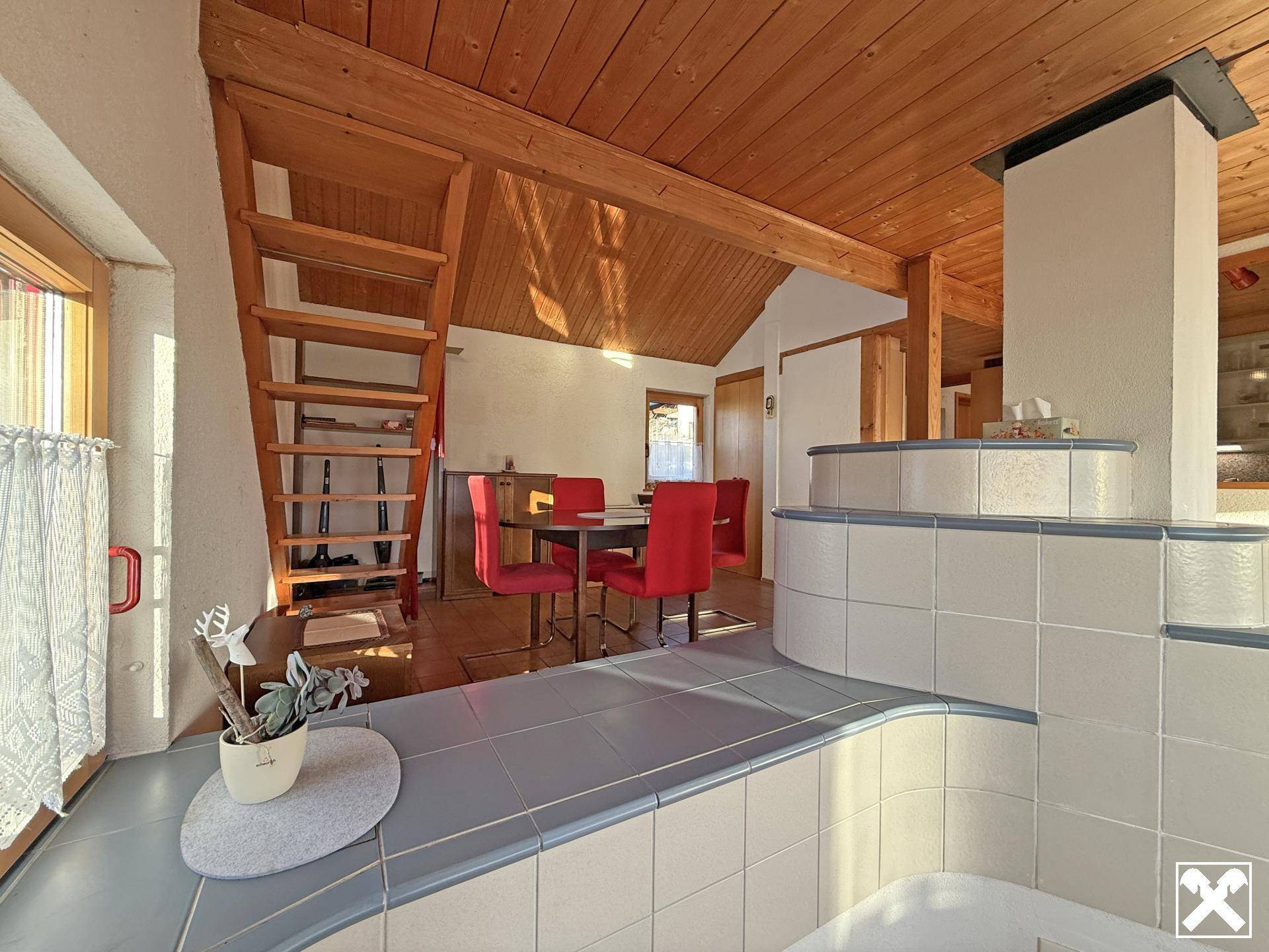 Gemütlicher Essbereich mit traditionellem Kachelofen, Holztreppe und Blick auf weitere Wohnbereiche.