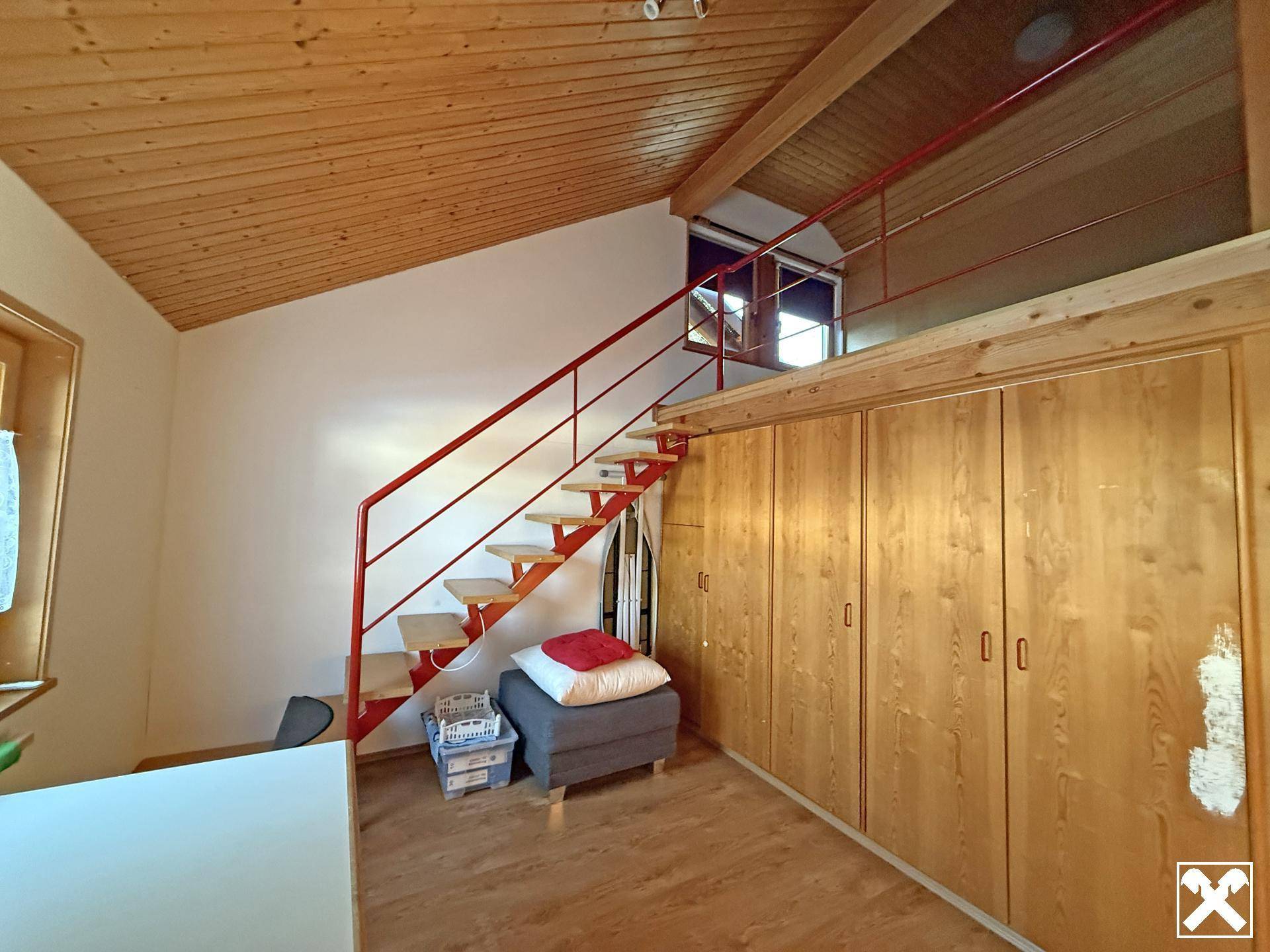 Schlafzimmer mit Holzdecke, Einbauschränken und einer roten Treppe, die zu einer oberen Ebene führt.