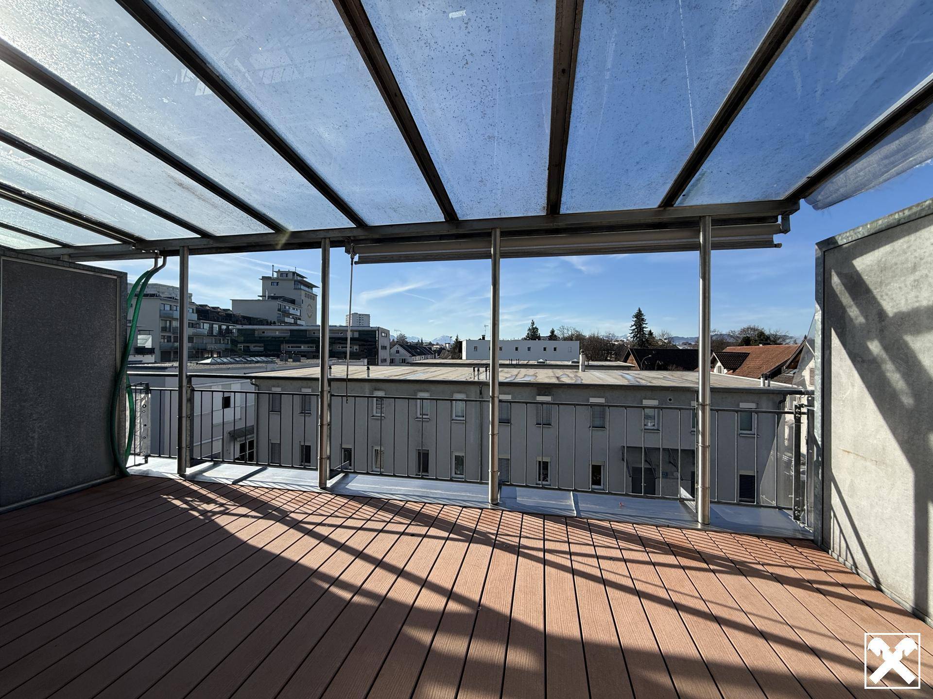 Sonnige Dachterrasse mit Holzboden, Glasüberdachung und weitem Blick über die Stadt.