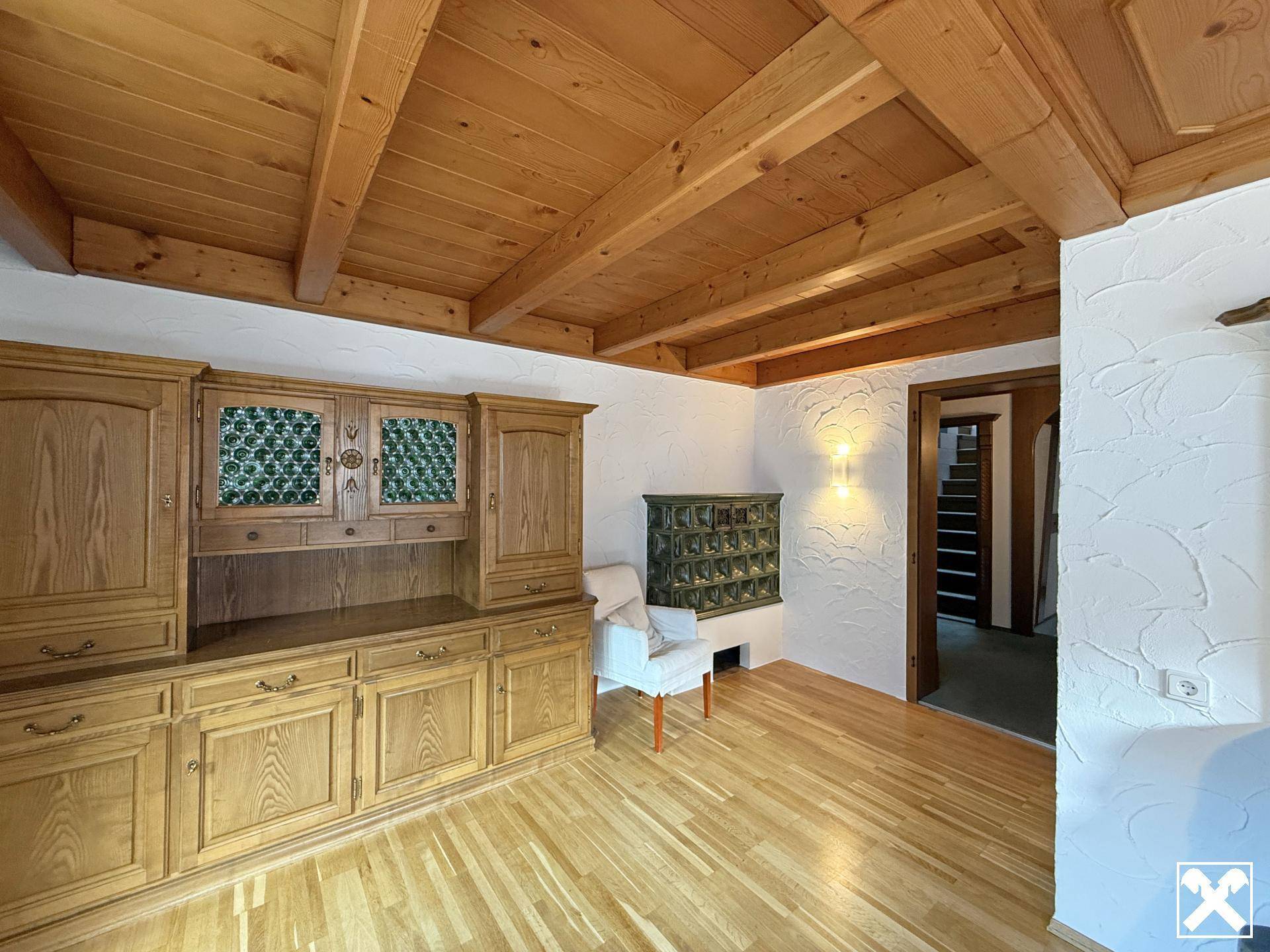 Wohnraum mit Holzbalkendecke, Parkettboden und traditionellem Kachelofen.