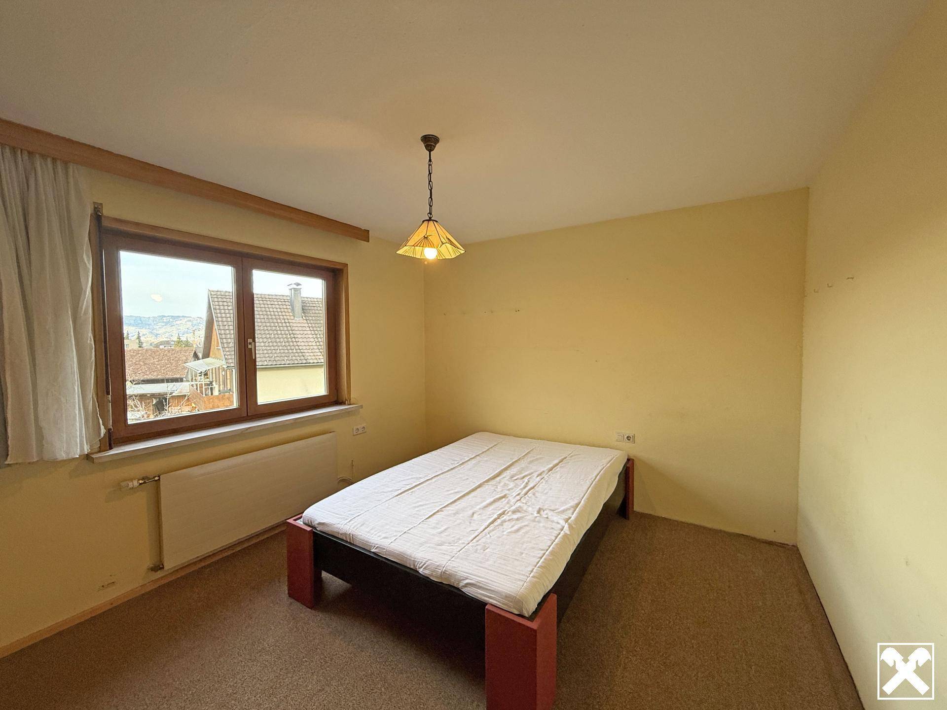 Einfaches Schlafzimmer mit Fenster und Teppichboden, bereit zur individuellen Gestaltung.