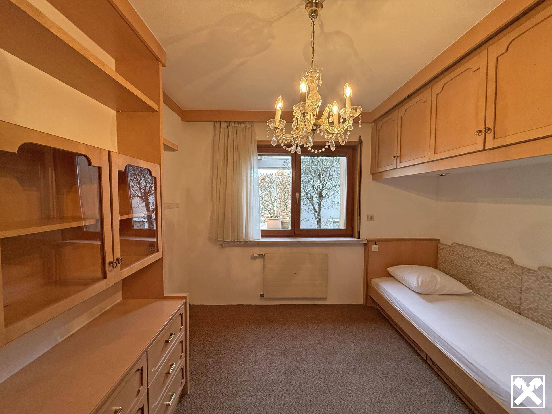 Helles Schlafzimmer mit Einzelbett, Einbauschränken und Kronleuchter.