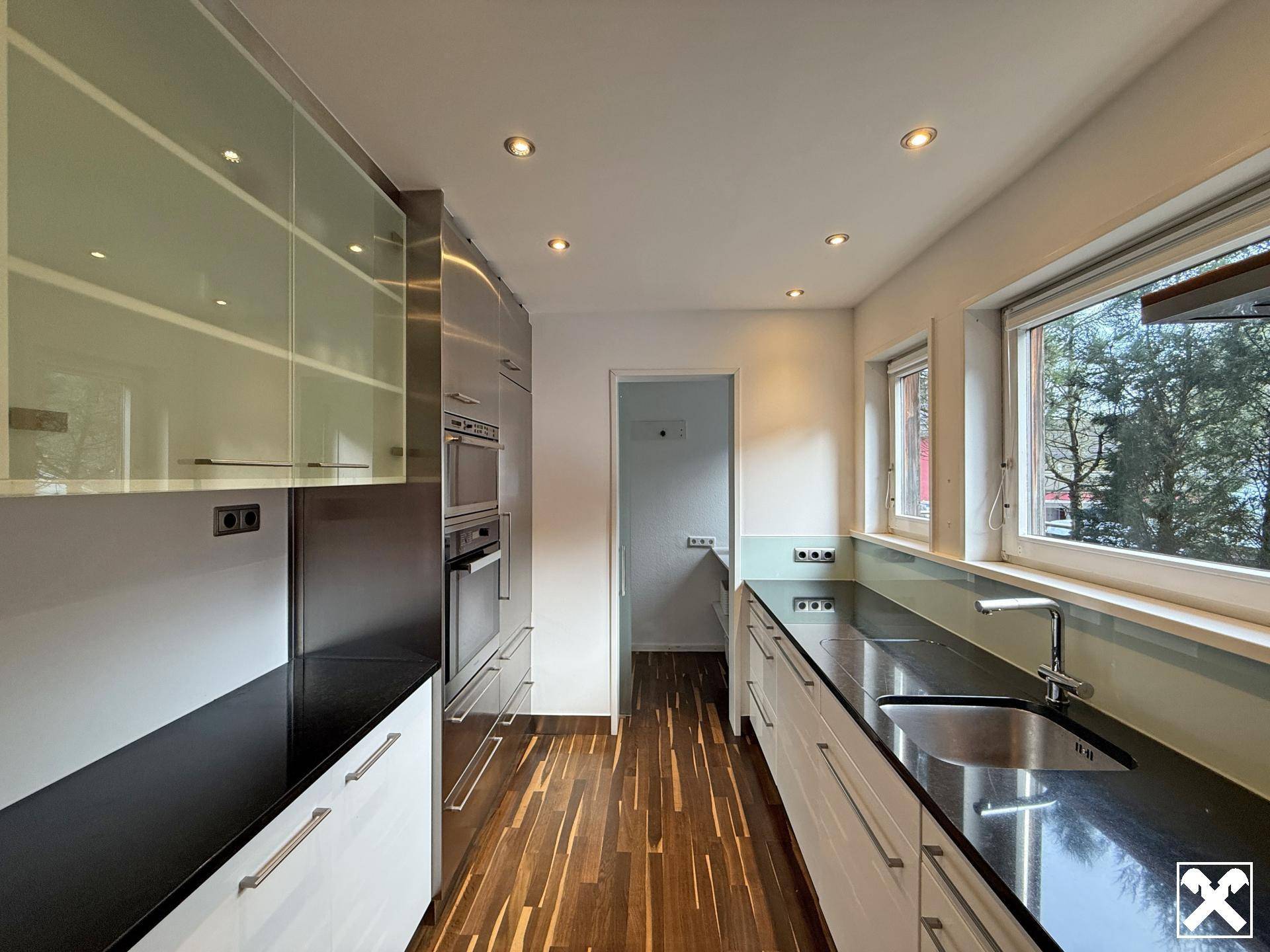 Moderne Küche mit dunklen Arbeitsplatten, integrierten Geräten und Holzboden.