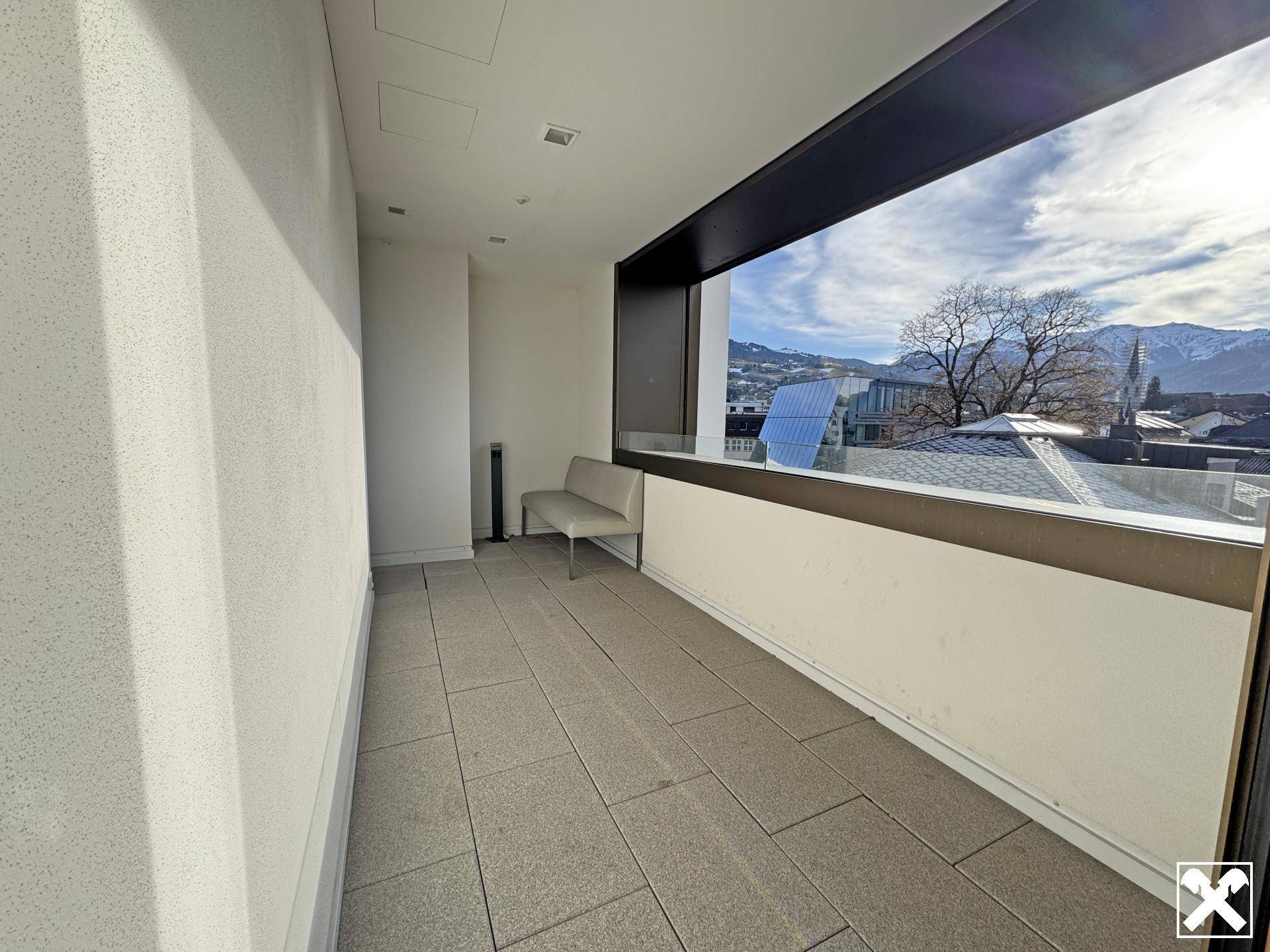 Überdachte Loggia mit Fliesenboden, einer Sitzbank und weitem Blick auf die Stadt und die Berge.
