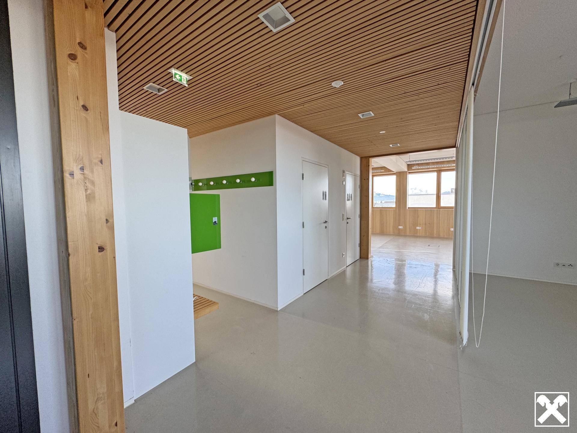 Moderner Eingangsbereich mit Holzlamellendecke, weiß gestrichenen Wänden und einem hellen Betonboden.