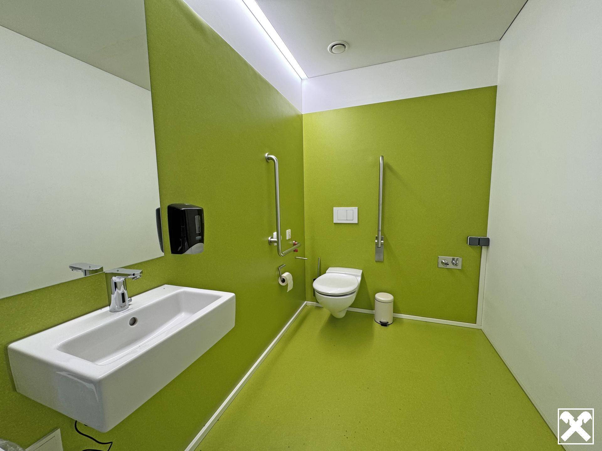 Modernes, barrierefreies Badezimmer in leuchtendem Grün mit Wand-WC und Haltegriffen.