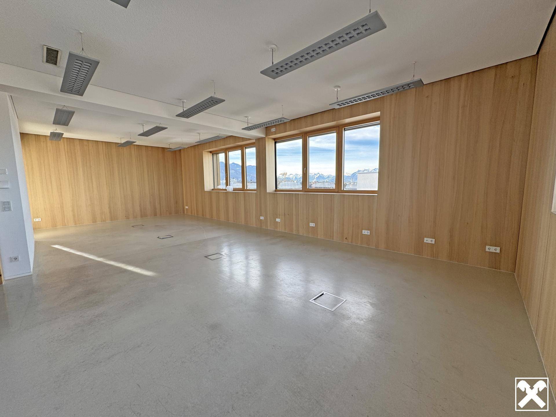 Weitläufiger Büroraum mit Holzverkleidung, großen Fenstern und einem klaren Blick auf die schneebedeckten Berge.