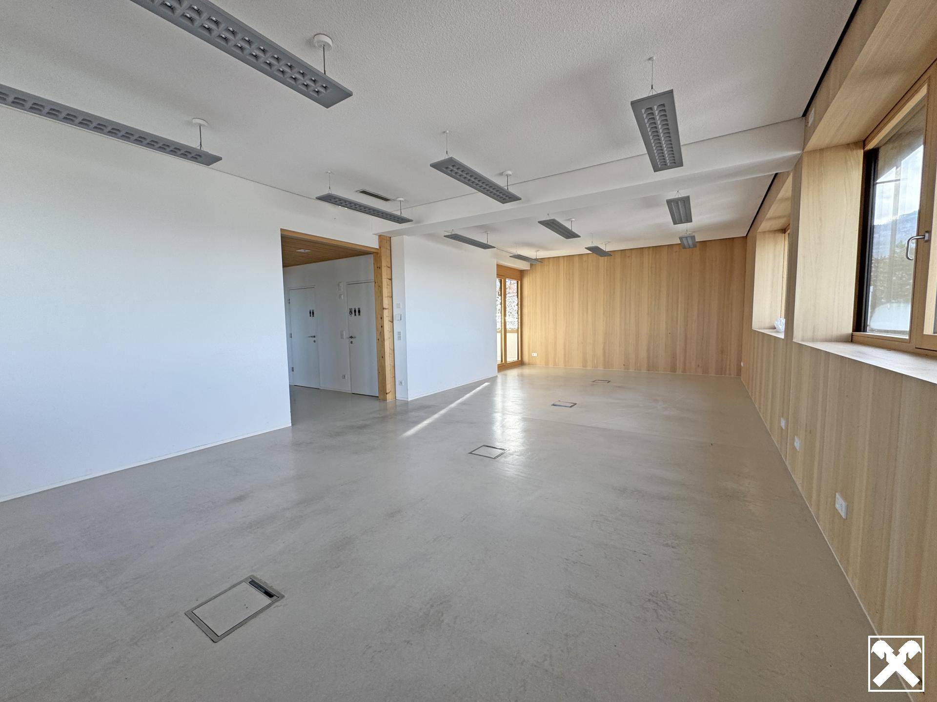 Geräumiger, heller Bürobereich mit Holzwänden, Betonboden und einem modernen, sauberen Erscheinungsbild.
