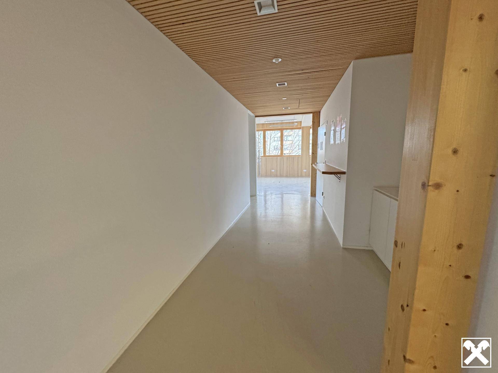 Langer, heller Flur mit Holzlamellendecke und weiß gestrichenen Wänden, der zu weiteren Räumen führt.
