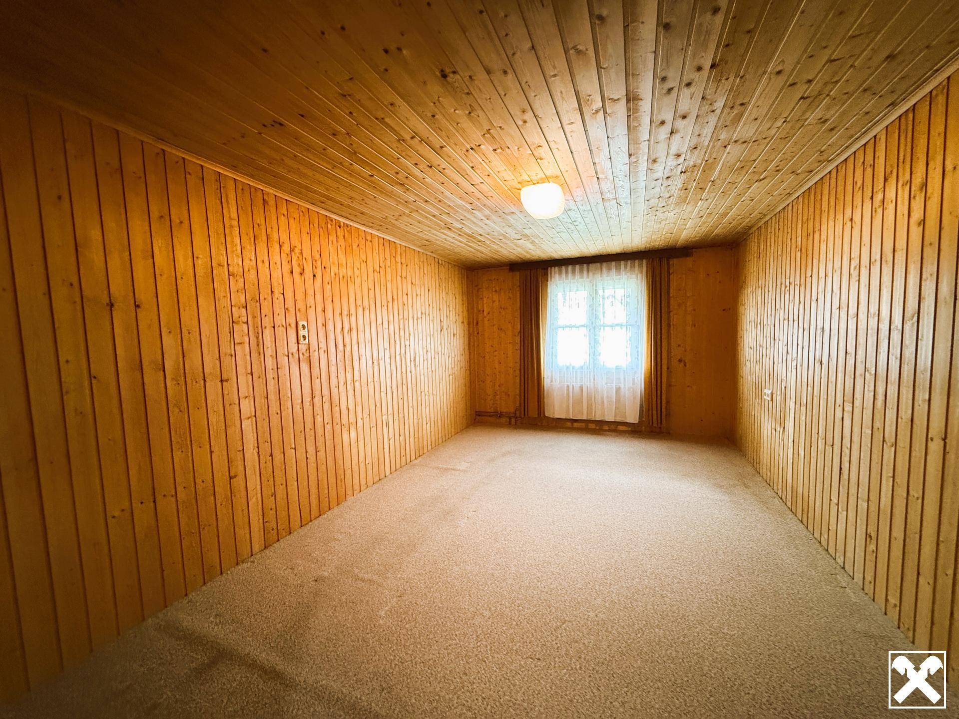 Gemütliches Schlafzimmer mit Holztäfelung an Wänden und Decke sowie Teppichboden.