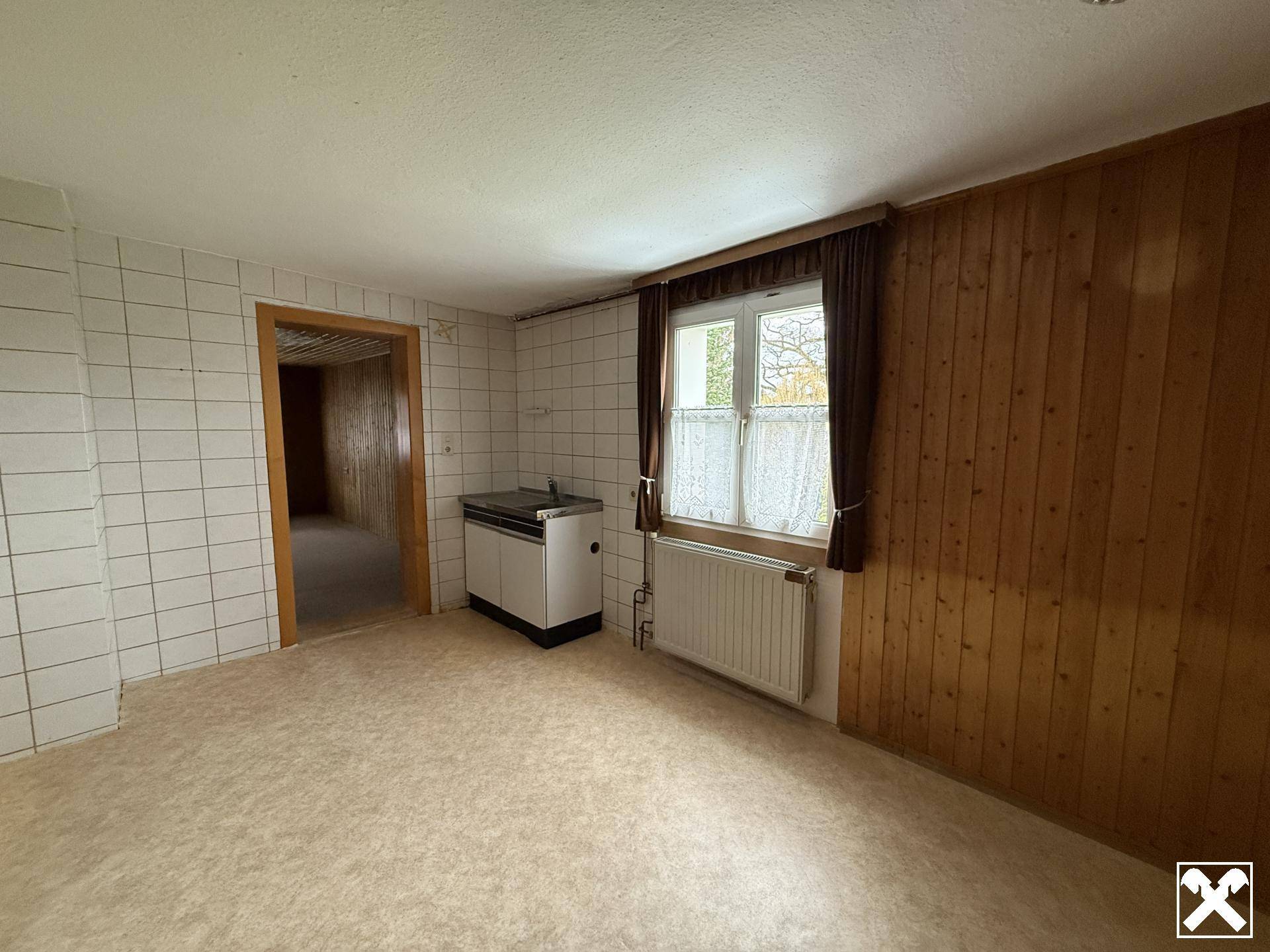 Einfache Küche mit weißen Fliesenwänden, Holztäfelung und einem Fenster.