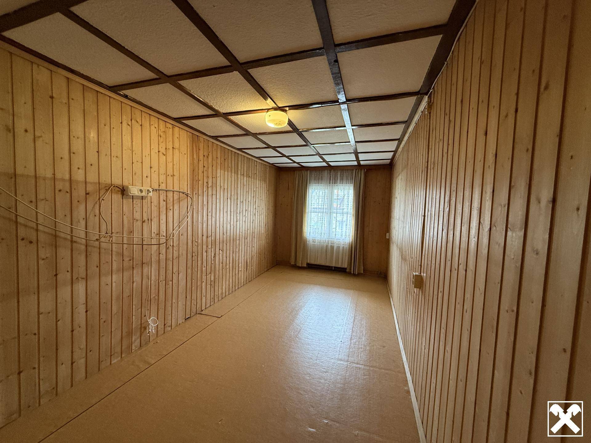 Schmaler Raum mit Holztäfelung, Vinylboden und einem Fenster mit Vorhängen.