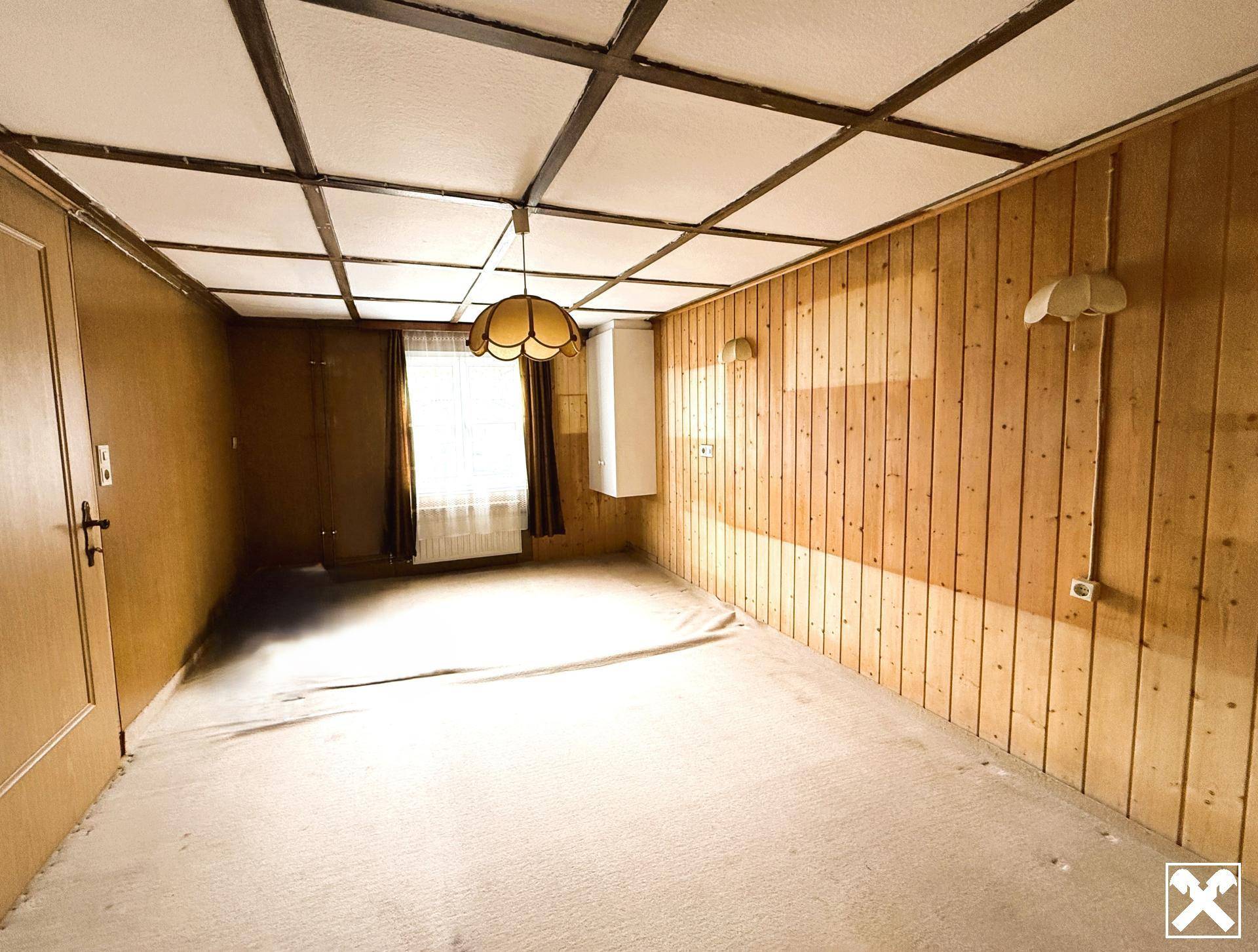 Heller Raum mit Holztäfelung, Teppichboden und einfacher Deckenbeleuchtung.