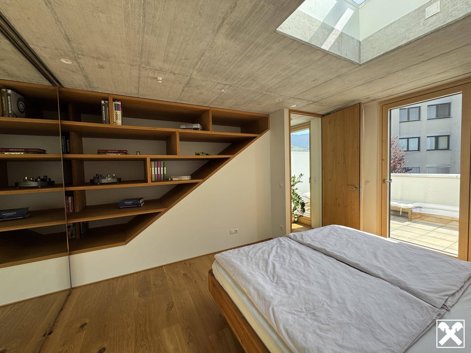 Schlafzimmer mit maßgefertigtem Holzregal, Holzboden und Zugang zur Terrasse.
