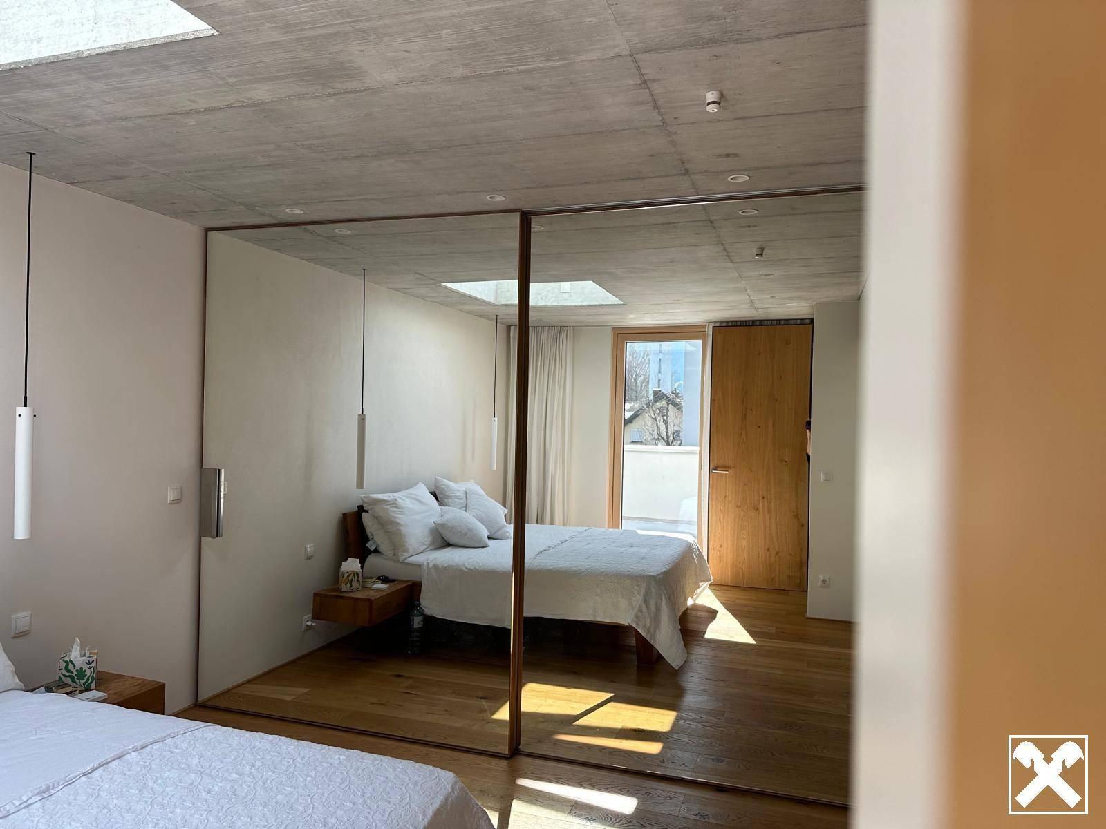 Helles Schlafzimmer mit Holzboden, Glaswand und Zugang zu einem Außenbereich.